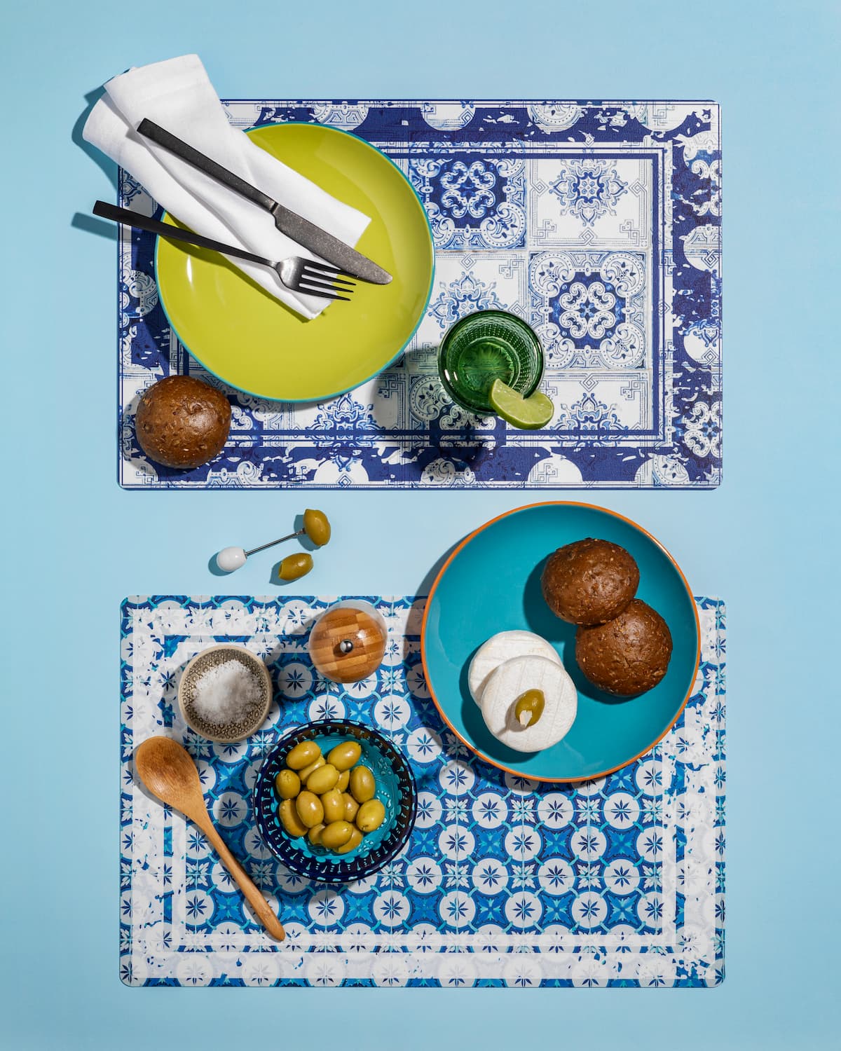tovagliette-americane-maiolica-piastrelle tovagliette americane in pvc grafica piastrelle blu con cibo mediterraneo olive pane mozzarella su tavolo azzurro